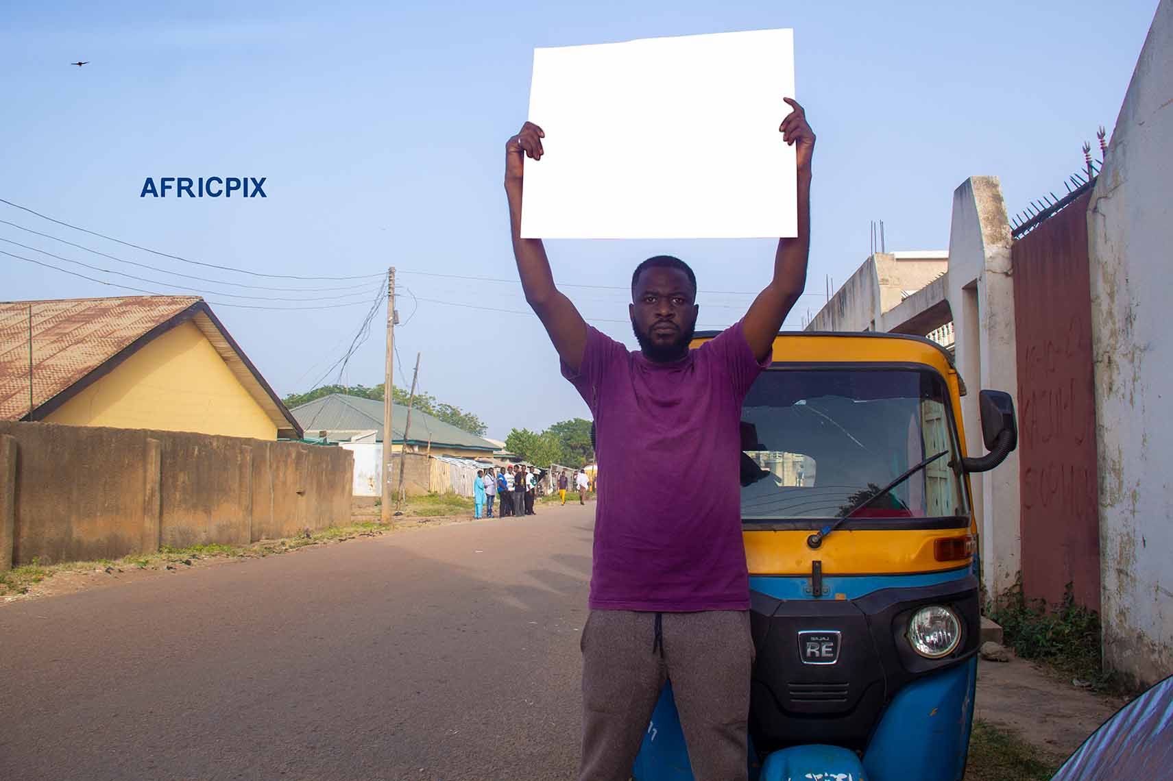 A Sad African tricycle rider, also known as Keke or Maruwa rider, standing with his tricycle behind him, holding a placard high over his head with an angry expression